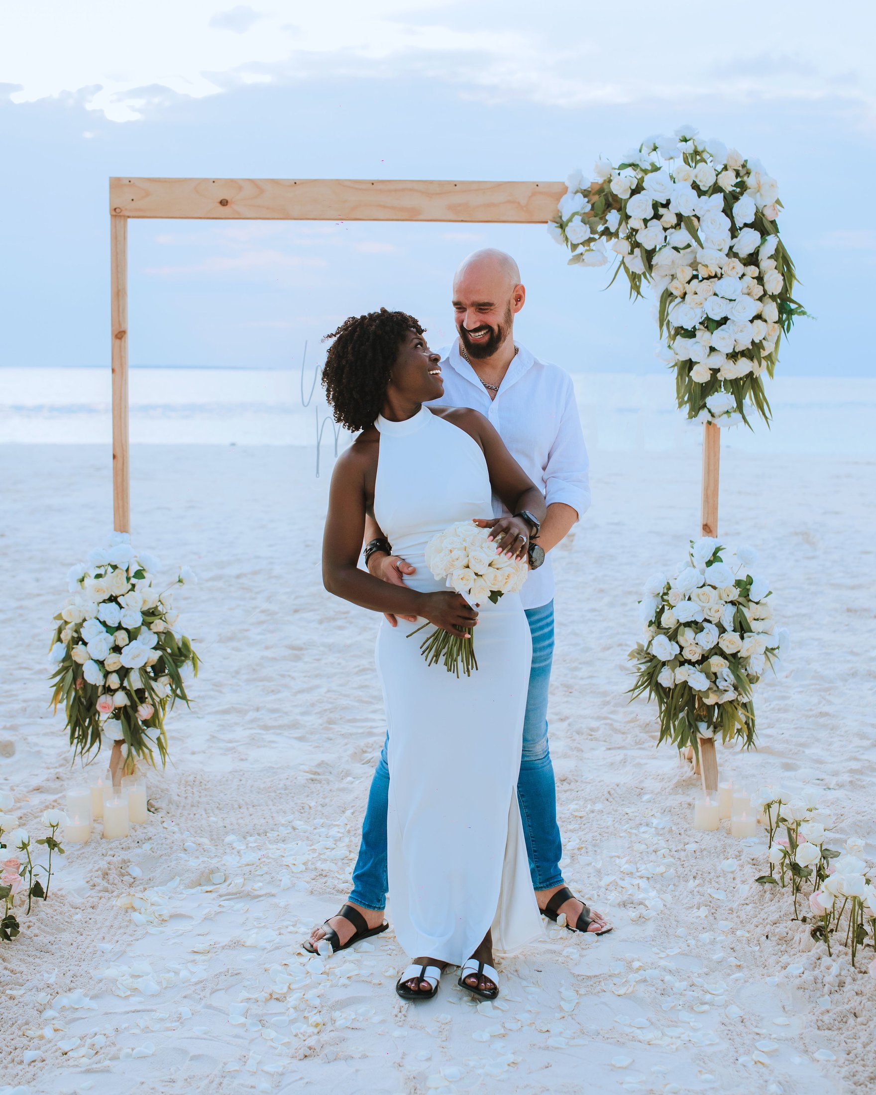 A couple celebrating between white floral arrangements on the beach