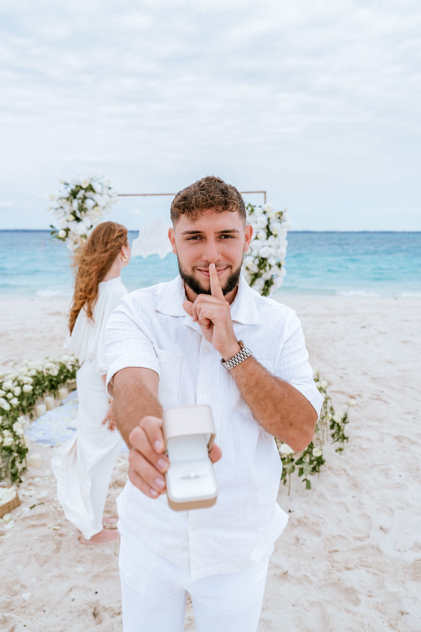 A joyful beach proposal beside white floral styling