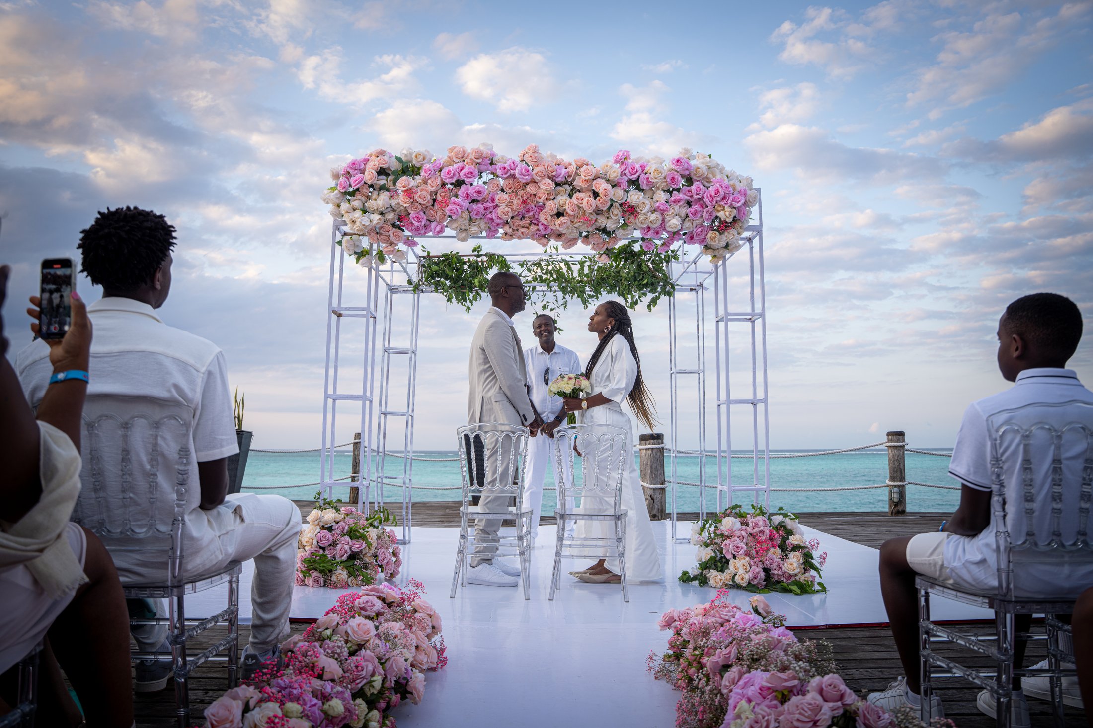 A seaside wedding ceremony framed by pink flowers