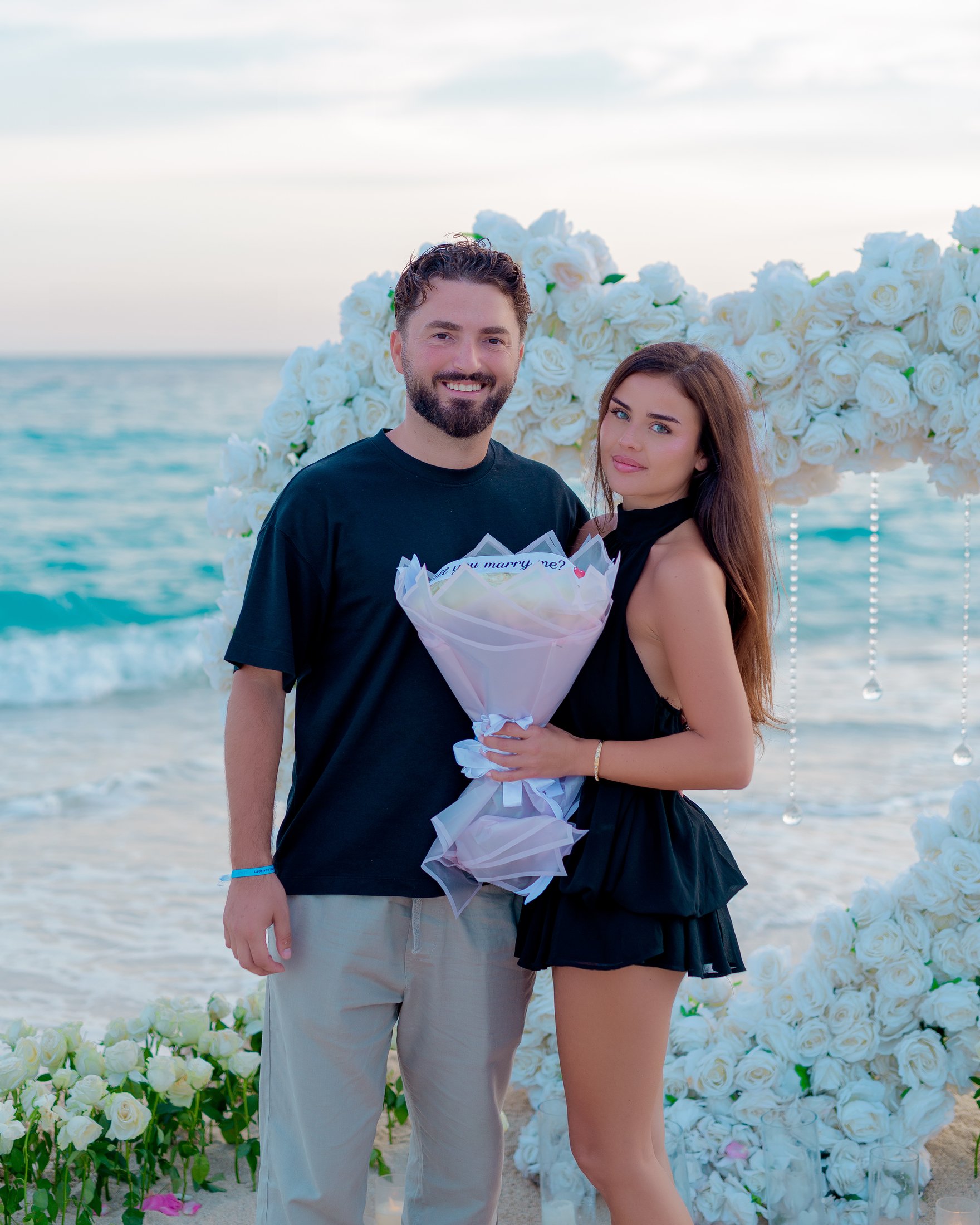 A couple holding flowers beside turquoise Zanzibar water